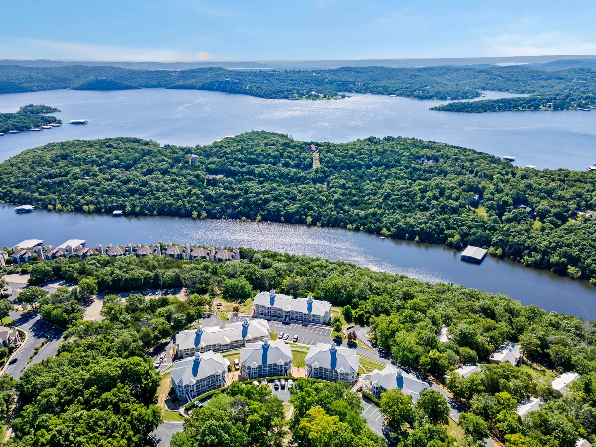 A tranquil lake stretches out beneath gently sloping hills, with residential buildings nestled in the background. The scene exudes stillness and invites thoughts of lakeside activities, sunset boat rides, and peaceful stargazing by the water.