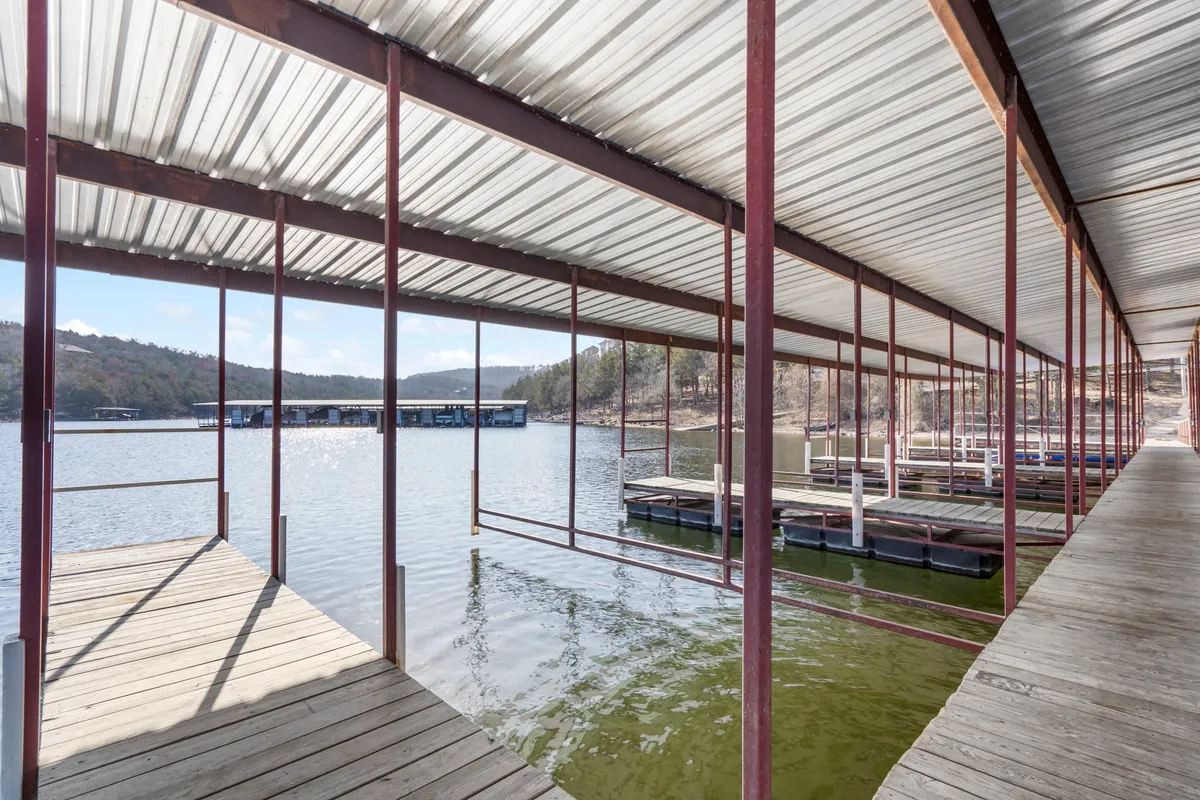 A tranquil scene featuring a wooden dock with multiple boat slips stretching into the calm waters of the lake, set against a backdrop of gentle mountains. The dock is clearly designed for boating and fishing, with ample space for boats to be moored. The peacefulness of the lake and the inviting dock make it perfect for launching water adventures or enjoying quiet moments by the water.