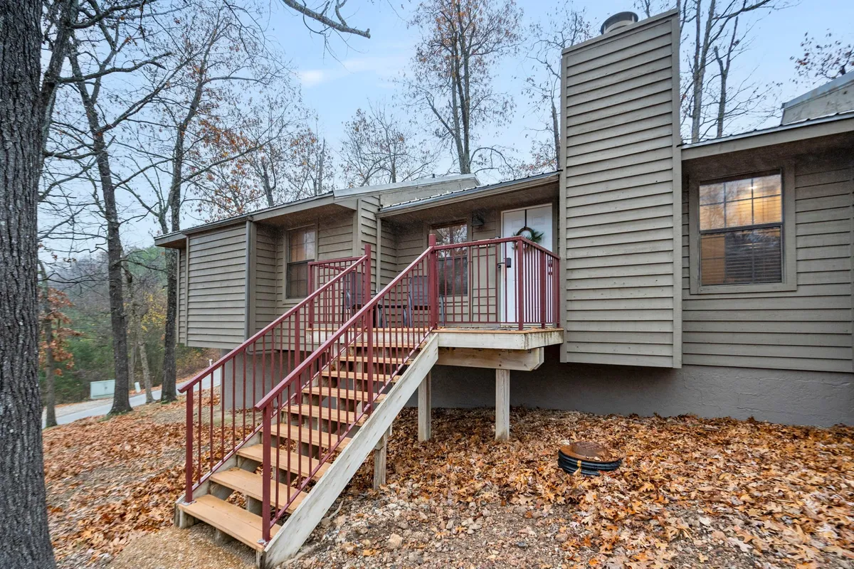 This image shows the welcoming entrance of the property featuring a wooden staircase with a red railing and an inviting entrance door. The setting is surrounded by greenery, suggesting easy access from outdoors for both guests and pets.