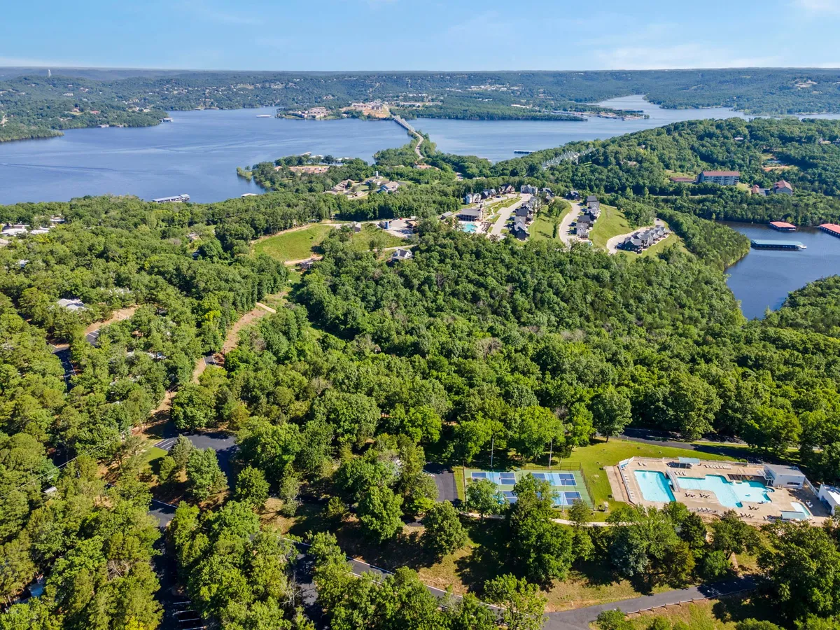 A panoramic view encompassing lush forests, a sparkling lake, a sparkling swimming pool, tennis courts, and a residential area. The setting is vibrant with recreational opportunities and natural beauty.