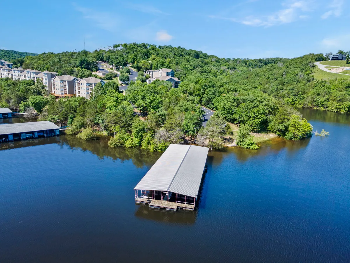 An exterior view capturing the tranquil lake, boathouse, and surrounding trees, with residential buildings visible. The area is ideal for walks, play, and lakeside adventures with pets.