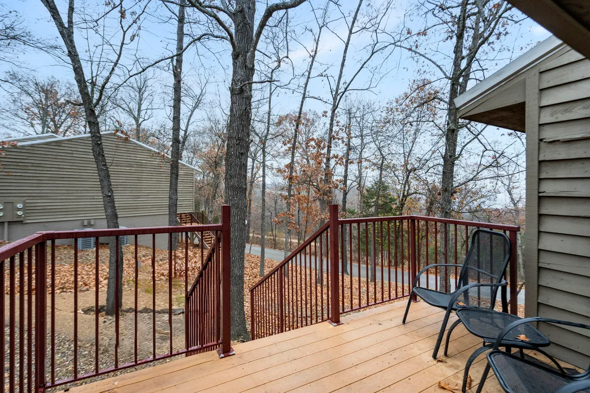 A tranquil private balcony scene with black chairs facing a lush, wooded backdrop. The wooden deck feels secluded and peaceful, ideal for morning coffee or evening toasts while enjoying the sights and sounds of nature and partial lake views through the trees.