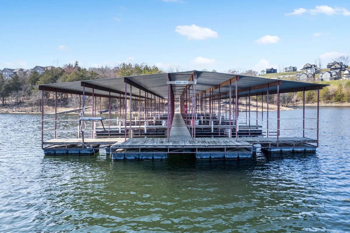 A serene exterior shot of a boat dock reaching out over calm water, surrounded by lush trees and gentle hills. The scene evokes early morning or evening, with soft light and tranquil reflections, suggesting moments of relaxation, fishing, or gathering with loved ones by the water.