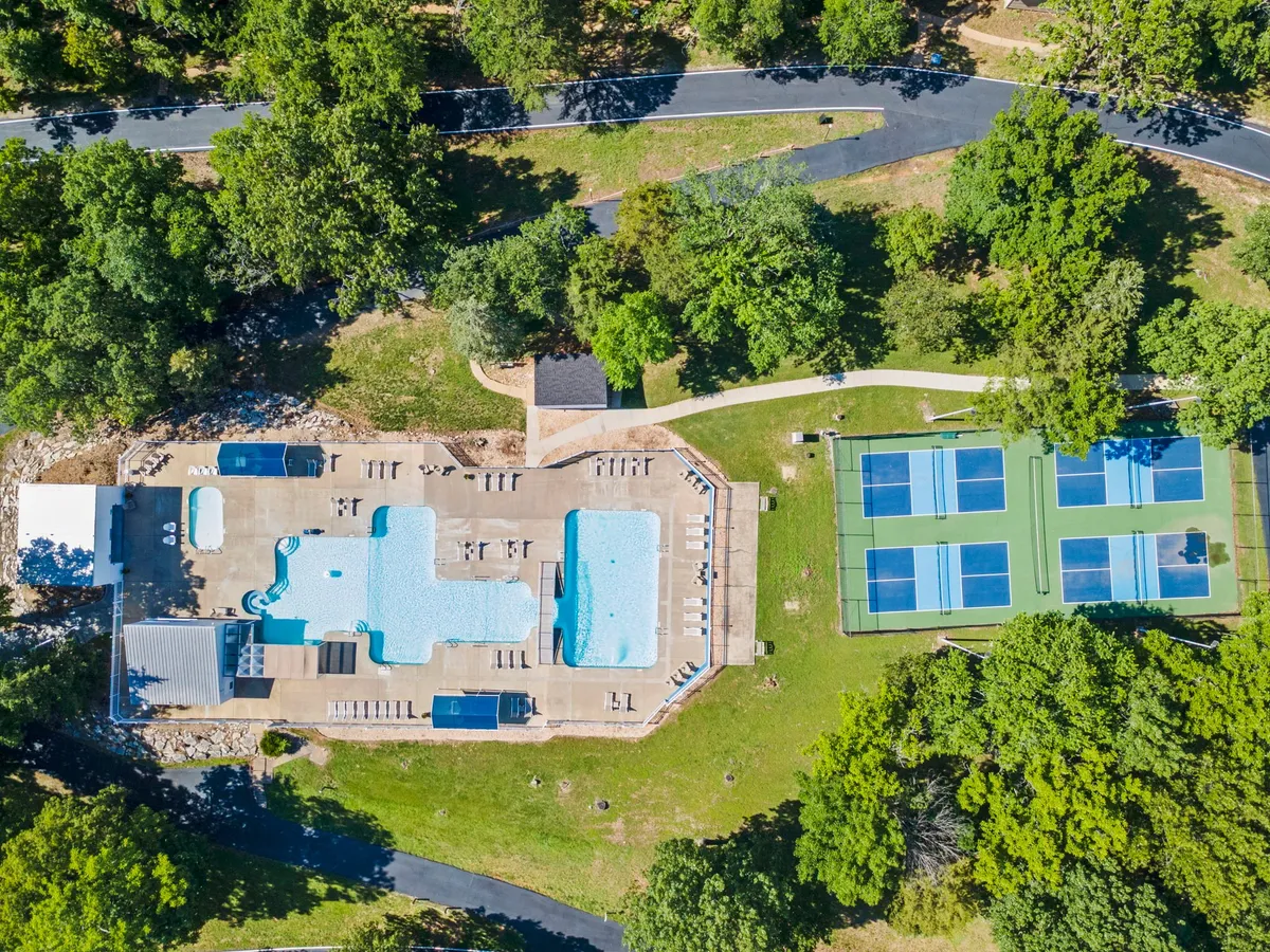This image features a swimming pool set among tennis courts and leafy green grounds. The area is bathed in natural light, inviting guests to swim, sunbathe, or take part in tennis matches, all within a vibrant outdoor setting.