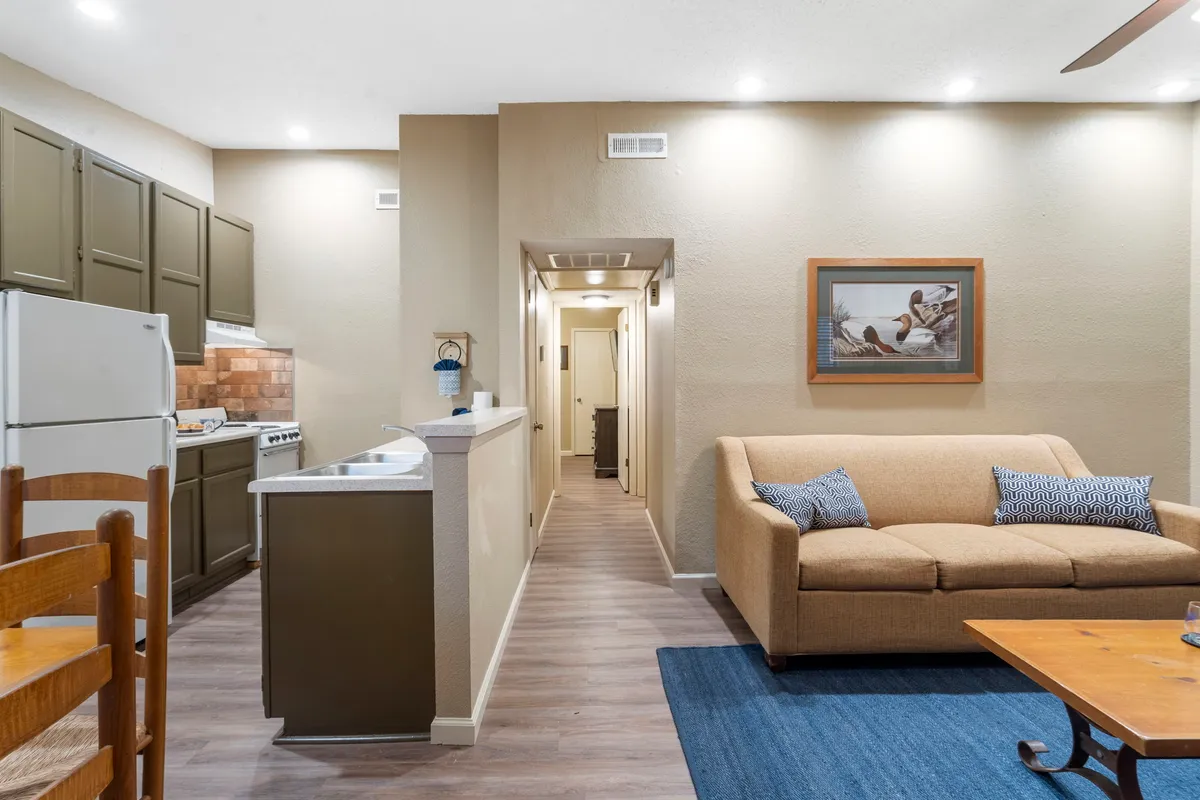 A cozy living area featuring a plush sofa (which doubles as a sleeper sofa), an open view to the kitchen and dining space, and inviting, homey décor. The room feels ideal for gathering or winding down after a full day.