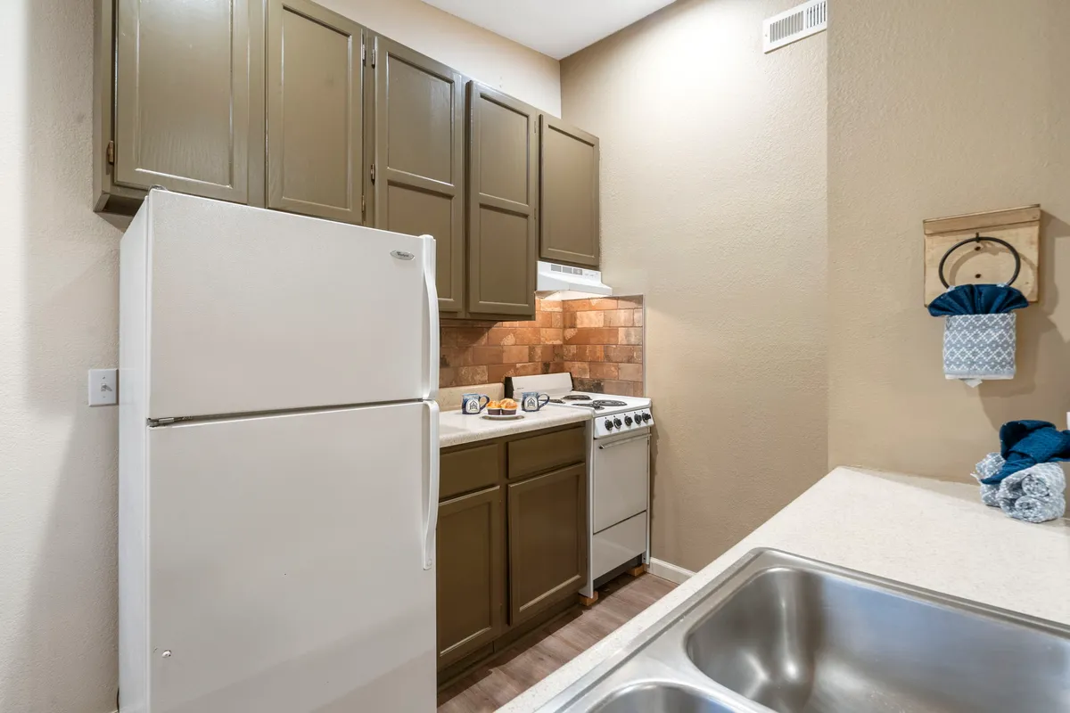A warm, homey kitchen scene with modern appliances including a refrigerator, stove, and sink. The countertops are organized for meal prep, and the setting suggests family or friends engaging in cooking and baking together.